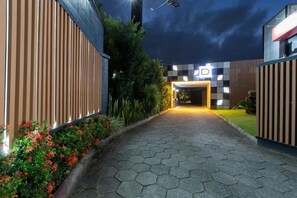 A pathway leading to a building with a modern design, featuring a geometric facade and a well-lit entrance. - Drops Motel Palhoça (Palhoça)