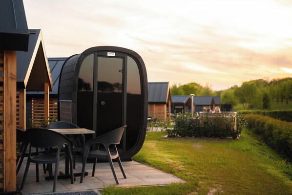 Un área de estar moderna al aire libre con una mesa, sillas, una estructura curva grande y un letrero que dice 'HOTUB'.
