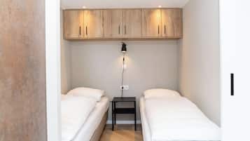 Een kleine, moderne slaapkamer met twee eenpersoonsbedden, een houten garderobe en een nachtkastje met een lamp.