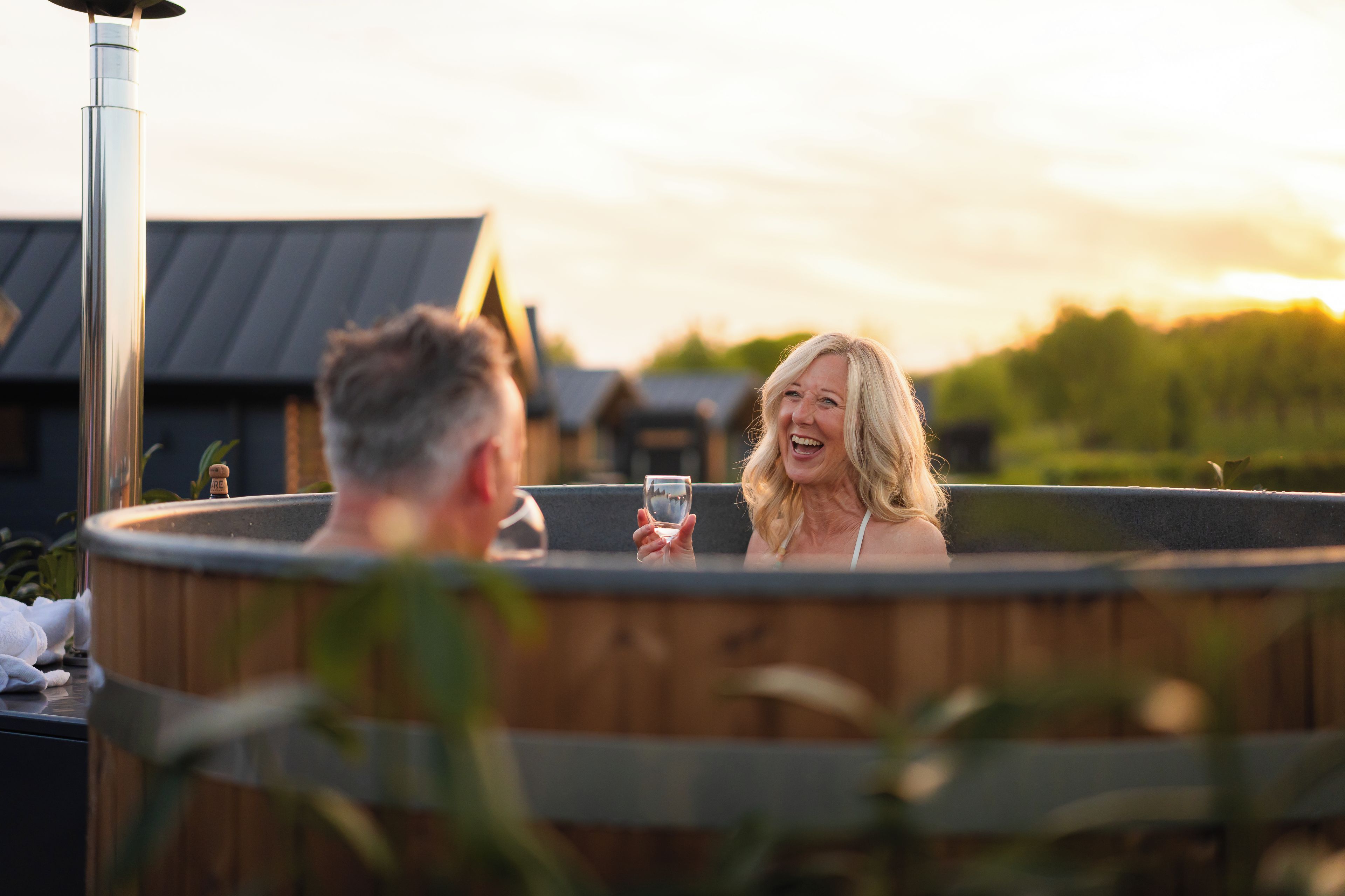 Ein Whirlpool mit Holzverkleidung, umgeben von Grünpflanzen und einem Haus im Hintergrund.