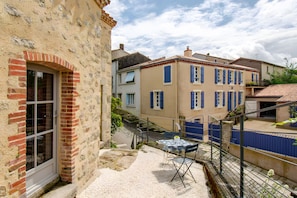 Une cour avec une table et des chaises, un mur de briques et un bâtiment aux volets bleus.