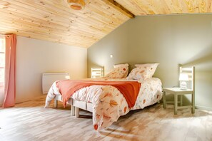A bedroom with a sloped ceiling, a bed with floral bedding, a bedside table with a lamp, and a window with curtains.