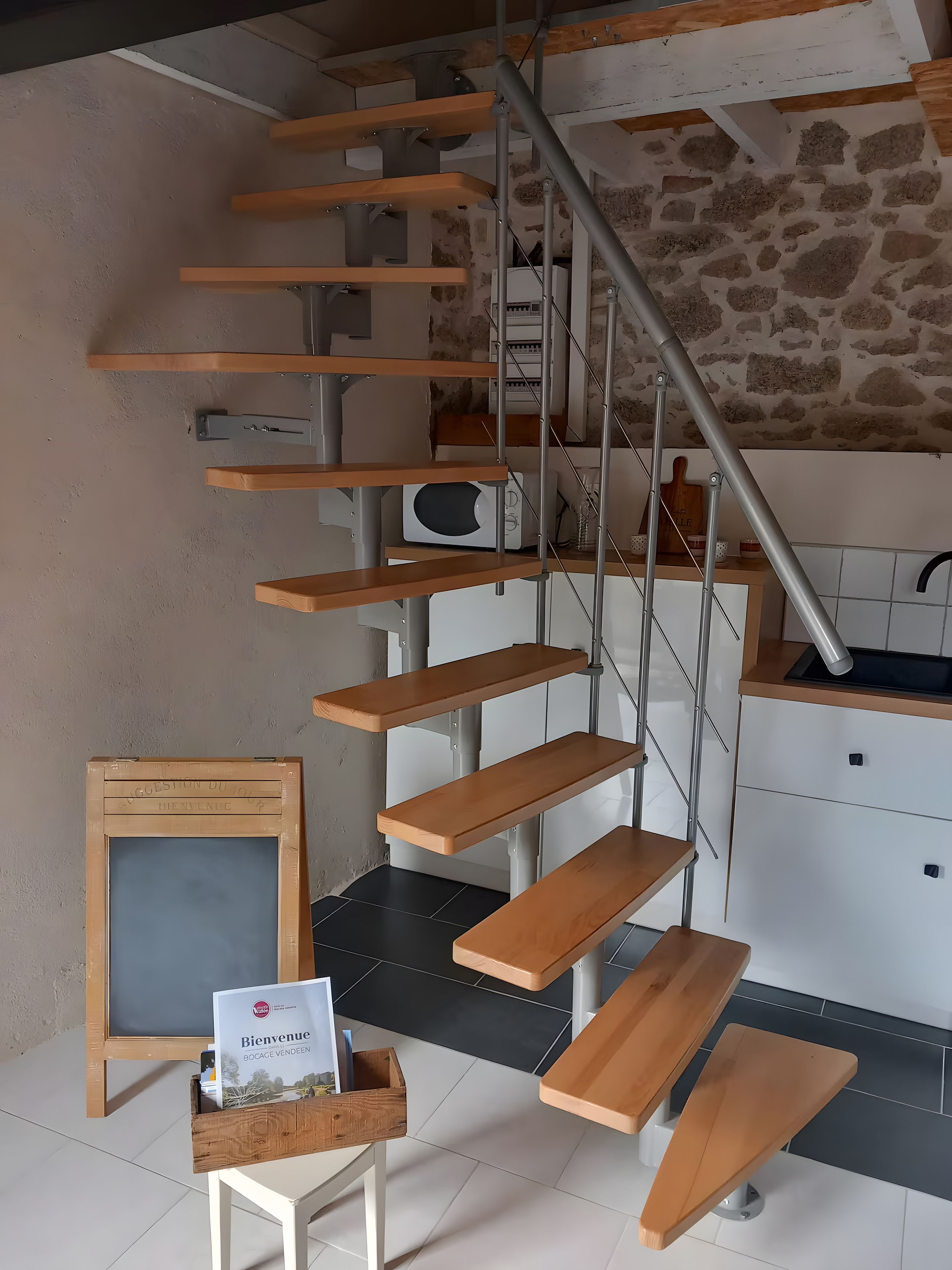 Un intérieur moderne agrémenté d’un escalier en colimaçon, d’étagères en bois, d’une pancarte d’accueil encadrée et d’une petite table sur laquelle est posée une brochure d’accueil.