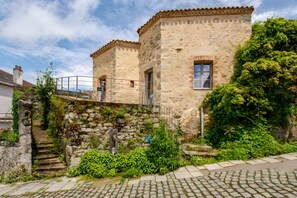 A stone building with a traditional design, a staircase leading to a door, and a garden area with greenery.