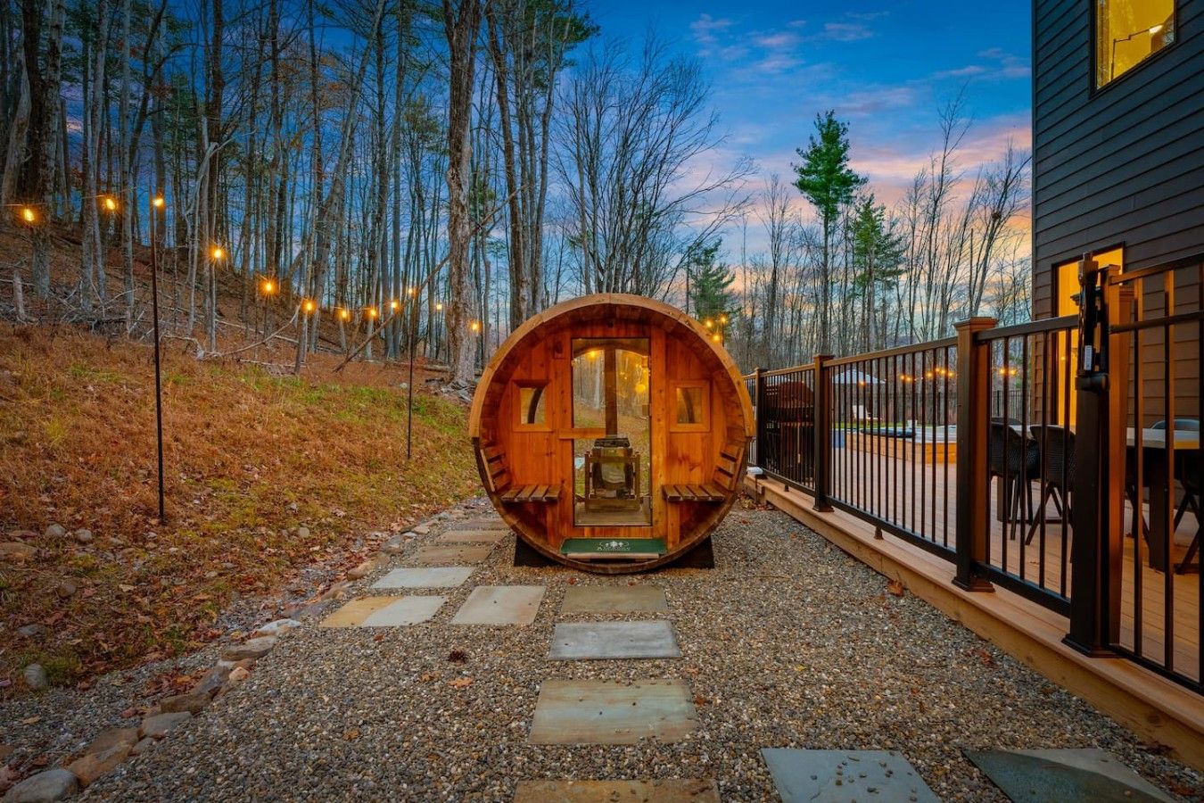 A wooden barrel-shaped structure with a bench inside, surrounded by a gravel path and a fence.