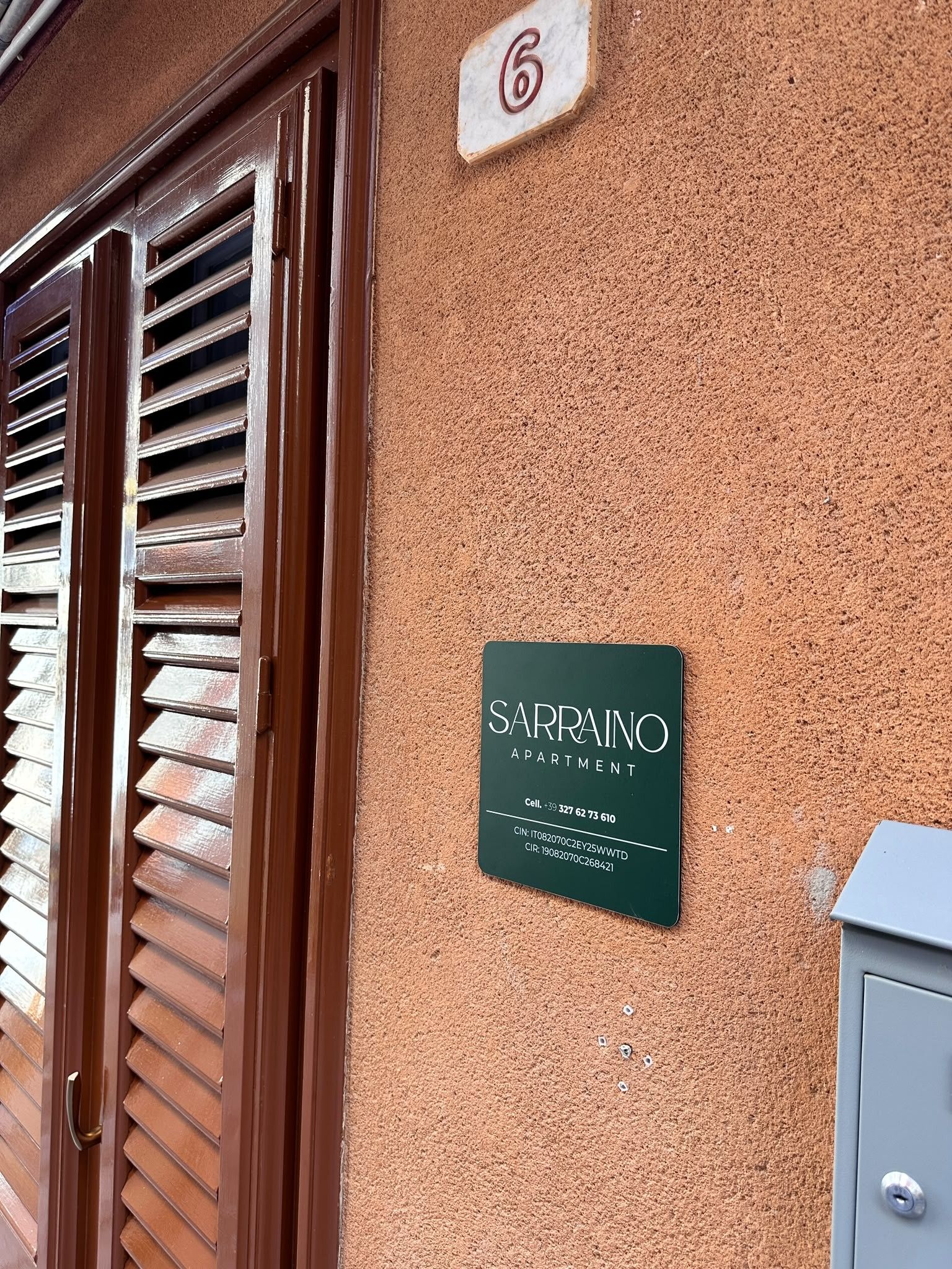 A building entrance with a wooden door and a sign indicating 'SARRANO APARTMENT' with contact information.