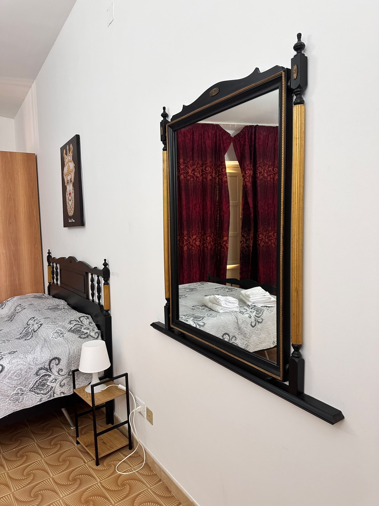 Ein Schlafzimmer mit einem Bett, einem Nachttisch mit Lampe, einem Spiegel und einem gerahmten Bild an der Wand.