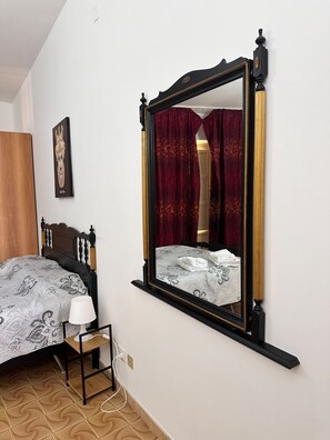 Ein Schlafzimmer mit einem Bett, einem Nachttisch mit Lampe, einem Spiegel und einem gerahmten Bild an der Wand.