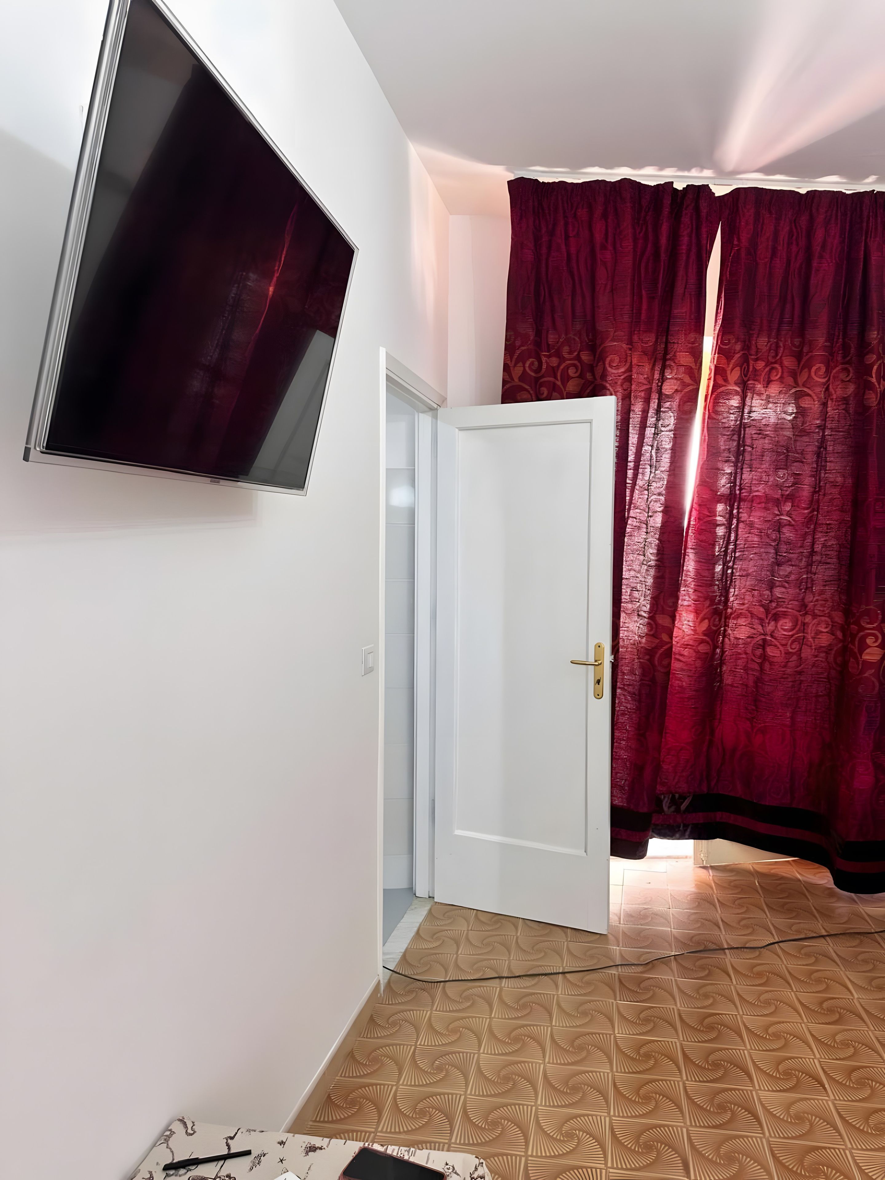 Ein Zimmer mit an der Wand befestigtem Fernseher, einer weißen Tür und einem gemusterten Boden.