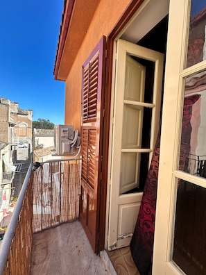 Ein Balkon mit Blick auf angrenzende Gebäude, eine Tür mit einem gemusterten Vorhang und eine Klimaanlage.