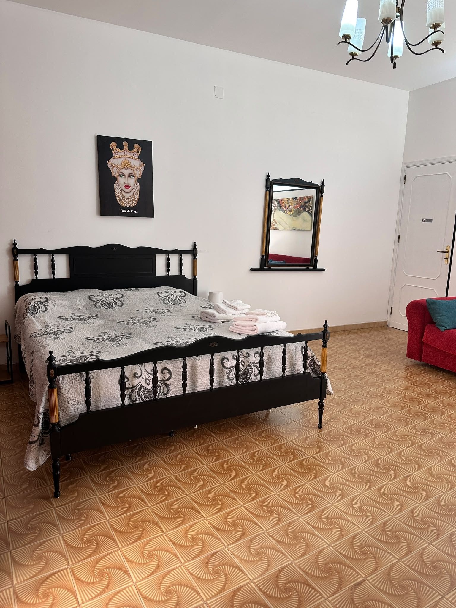 A bedroom with a bed, a painting, a mirror, and a door.