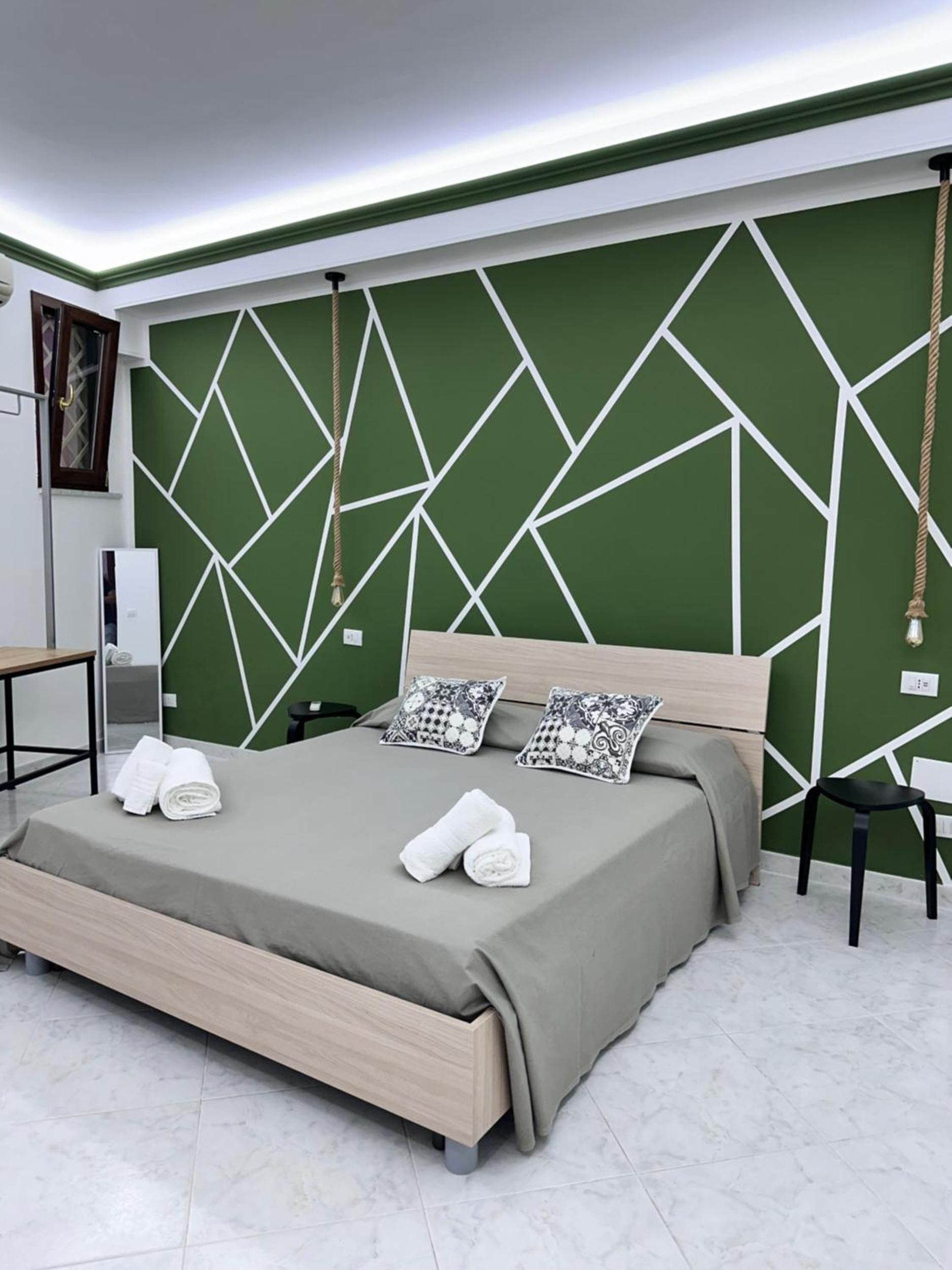 Ein modernes Schlafzimmer mit einem Kopfteil im geometrischen Muster, einem Bett mit grauer Bettdecke, zwei Kissen und ordentlich gefalteten Handtüchern auf dem Bett.
