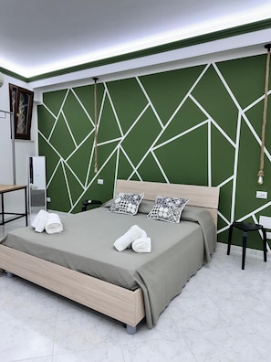Ein modernes Schlafzimmer mit einem Kopfteil im geometrischen Muster, einem Bett mit grauer Bettdecke, zwei Kissen und ordentlich gefalteten Handtüchern auf dem Bett.
