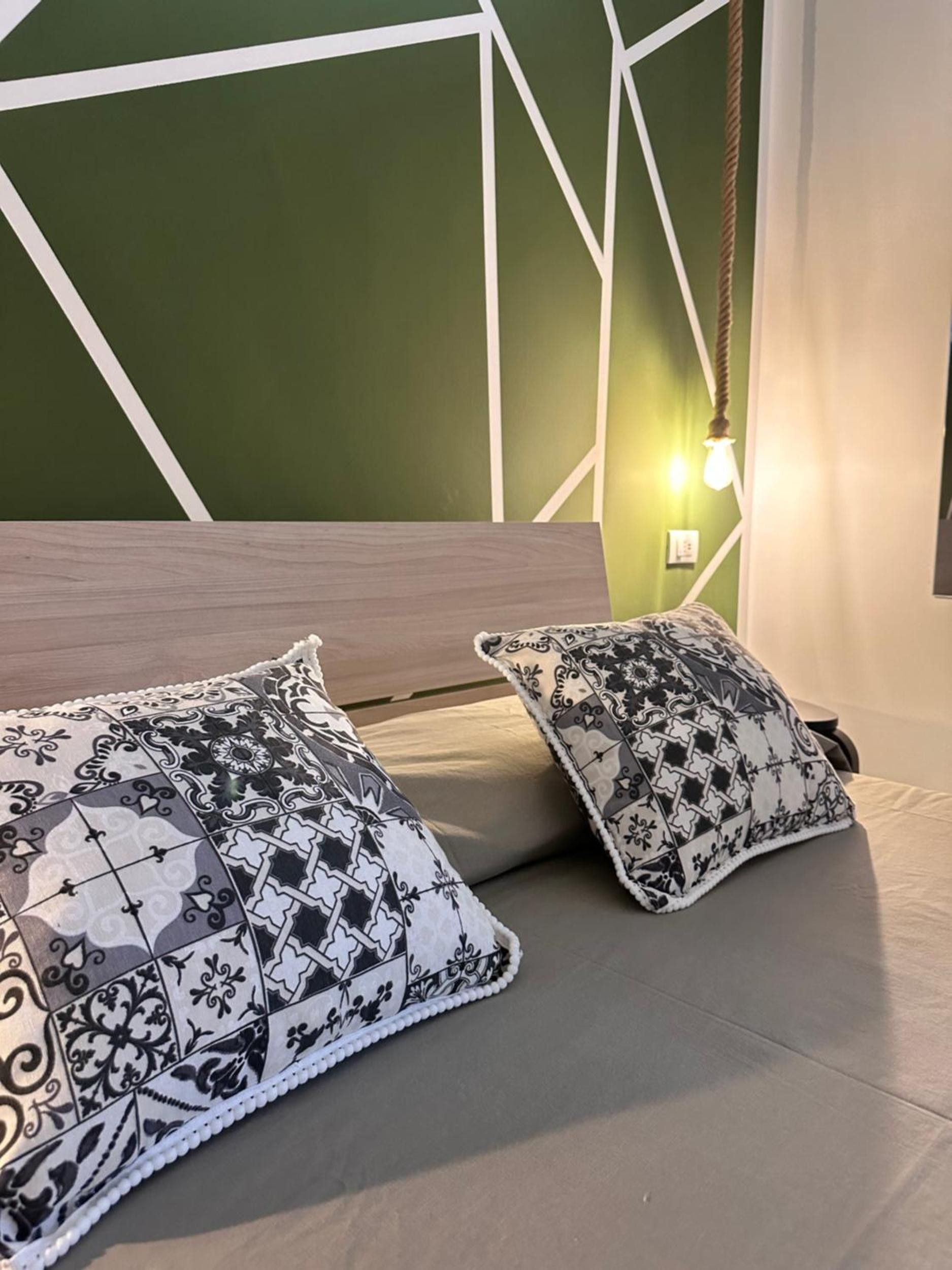 Sängyssä on kuvioituja tyynyjä ja seinässä geometrinen kuvio.