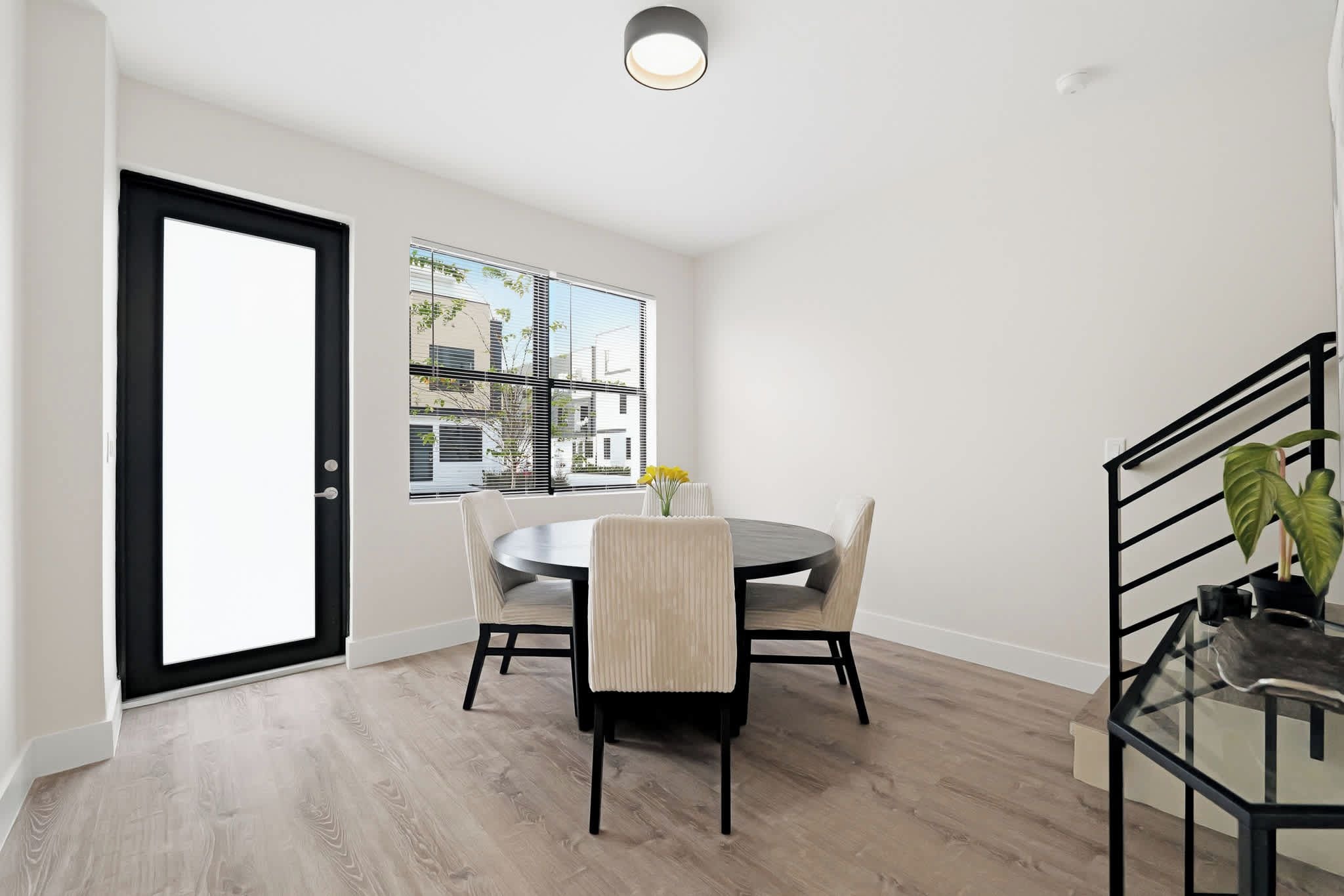 A dining area with a round table, chairs, a window with blinds, and a view of buildings outside.