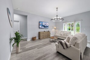 A modern living room with a sofa, a coffee table, a TV mounted on the wall, and a large window. - Gulf Coast Escape | Spacious 4BR Home for 9 (Port Charlotte)
