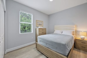 A bedroom with a bed, bedside tables, a nightstand, a window with blinds, and a wall-mounted picture.