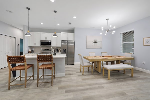A modern kitchen with white cabinets, stainless steel appliances, and a dining area with a wooden table and chairs. - Gulf Coast Escape | Spacious 4BR Home for 9 (Port Charlotte)