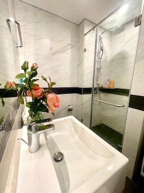 A bathroom with a white sink, a glass shower enclosure, and a vase of flowers on the sink. - Sweet Homes Tay Ho (Ha Noi)