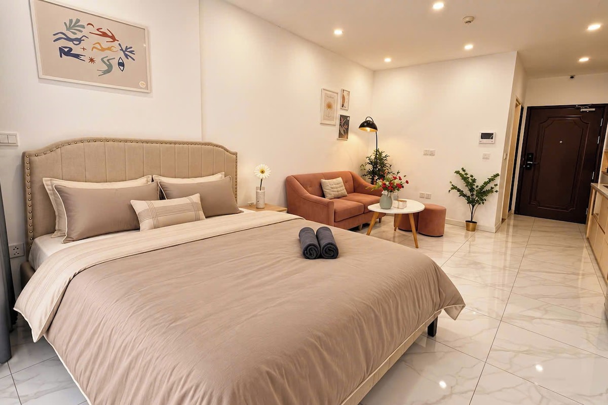 A hotel room with a large bed, a sofa, a small table, and a kitchen area.