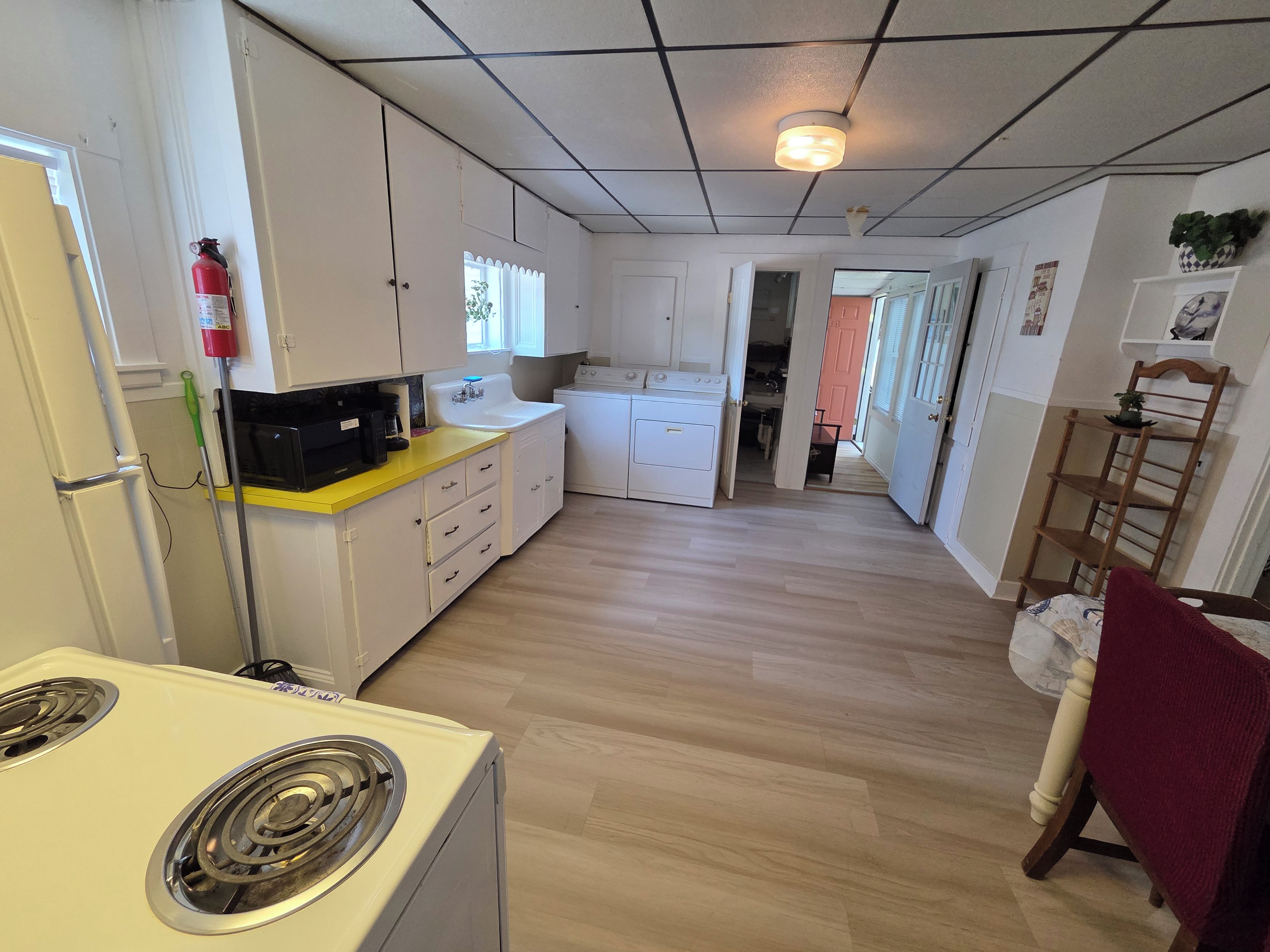 A compact kitchen with a microwave, sink, and stove. There is a fire extinguisher on the wall and a small window.
