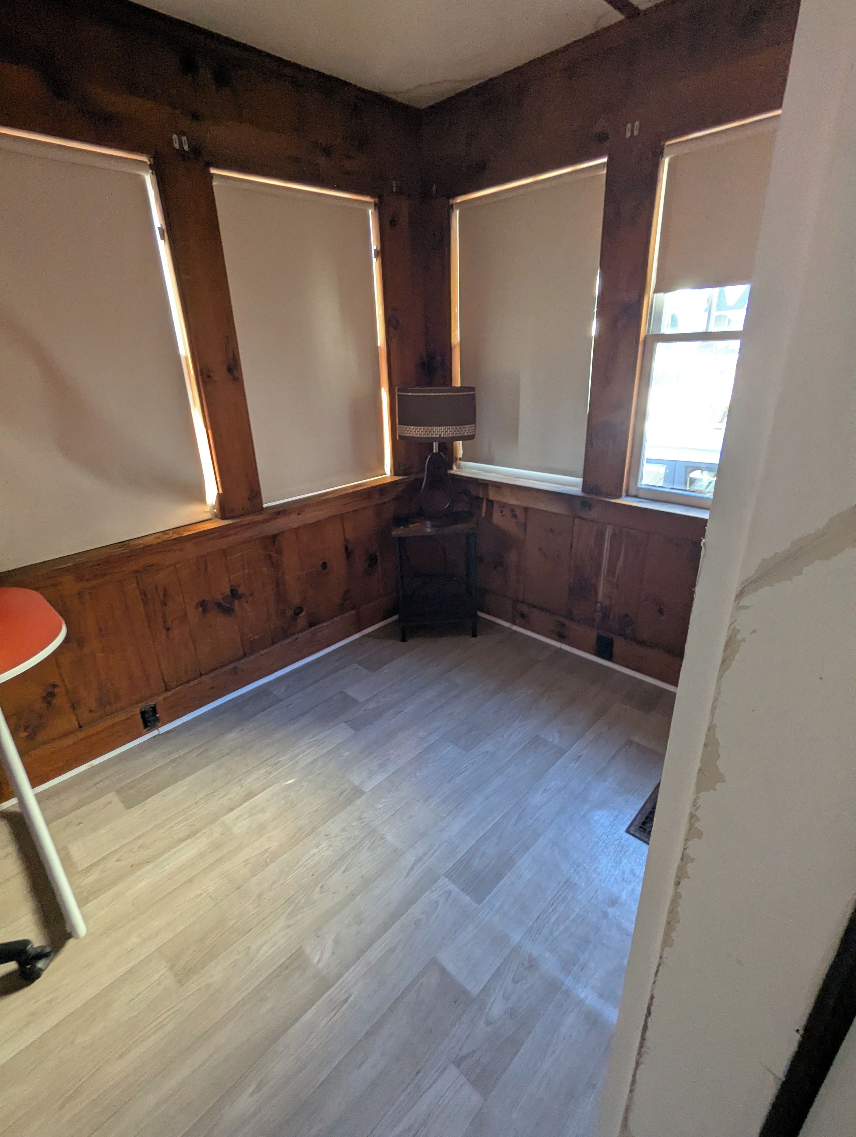 Una habitación con paredes de madera, suelo con estampado tipo espiga, una mesa y una silla.