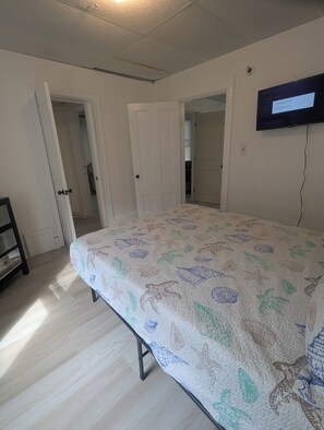Quarto com uma cama, televisão na parede e porta para outro cômodo.