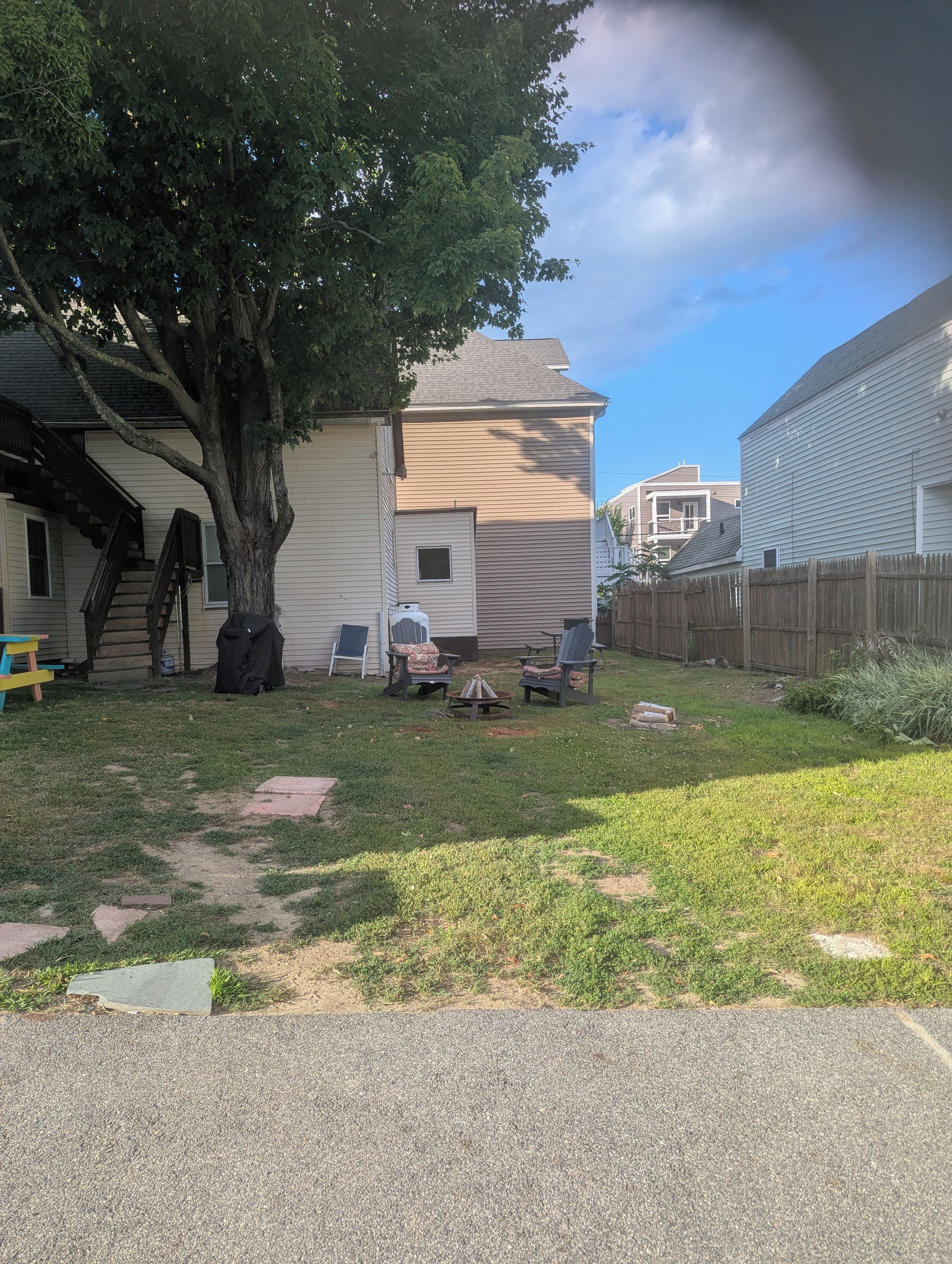 A residential backyard with a tree, a barbecue grill, and outdoor seating.