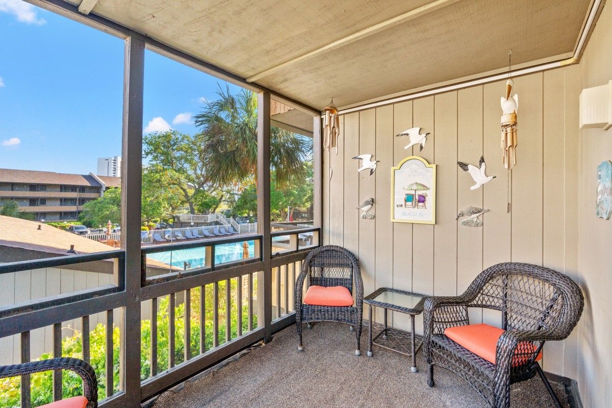 A balcony with wicker chairs, a small table, and a view of a swimming pool.