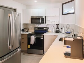 A modern kitchen with stainless steel appliances, a microwave, a toaster, and a coffee machine. - Urban Nest Lomas, 3 hab., vistas panorámicas, AC, balcón y 2 parqueos (San Salvador)