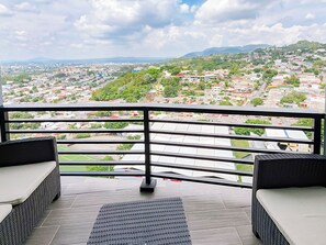 A balcony with a view of a cityscape, including buildings and greenery. - Urban Nest Lomas, 3 hab., vistas panorámicas, AC, balcón y 2 parqueos (San Salvador)