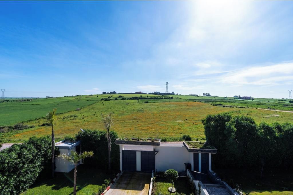 A residential property with a large open field, a small building with a garage, and a clear sky.