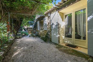 A gravel pathway leading to a house with a stone wall and a wooden pergola.