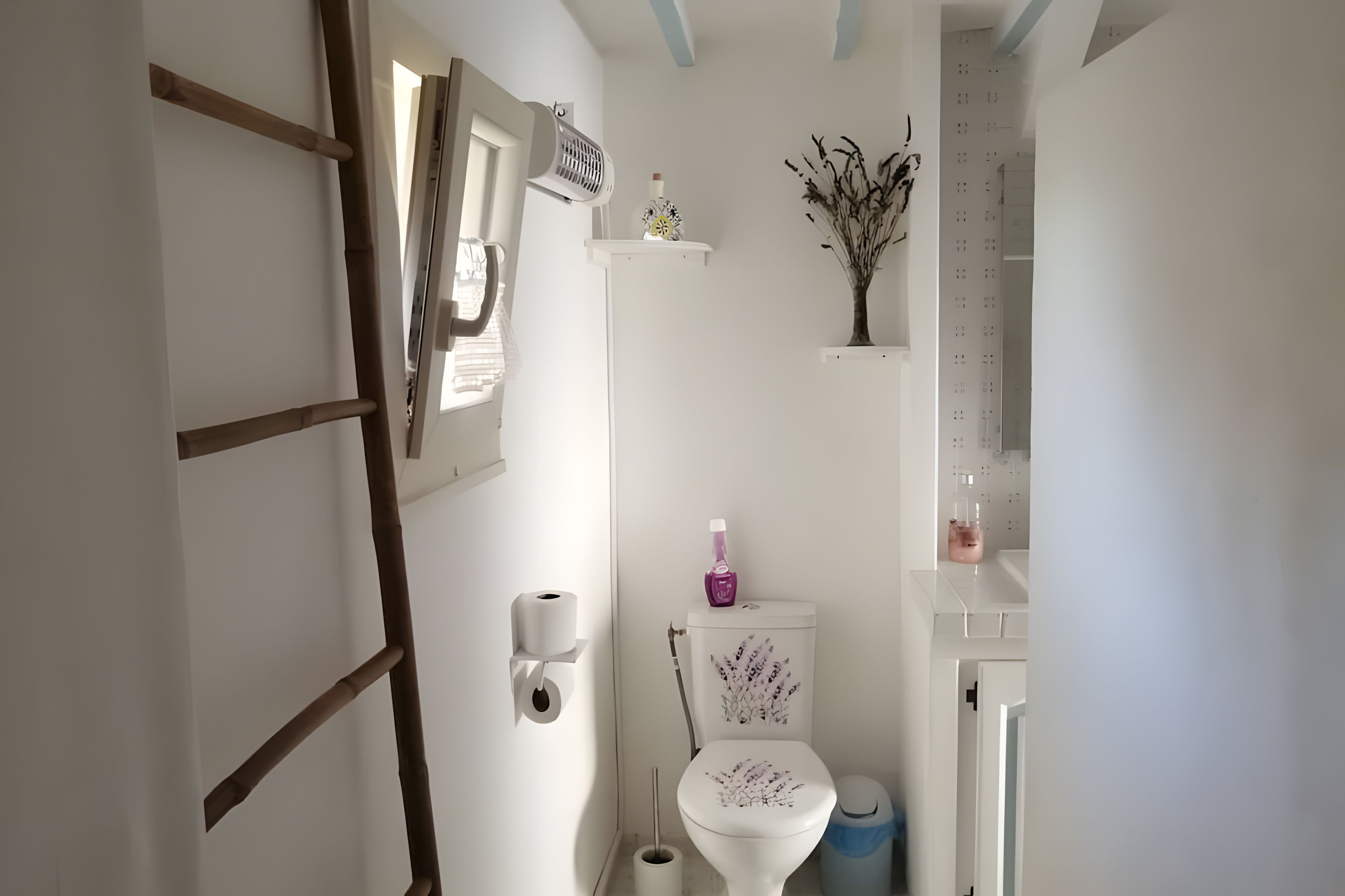 Een badkamer met een toilet, een handdroger, een papieren handdoekdispenser, een klein schapje met decoratieve objecten en een toiletborstel.