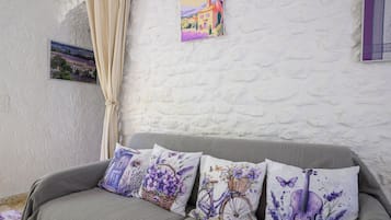 Une pièce avec un canapé gris, un mur blanc à texture et une fenêtre avec un rideau.