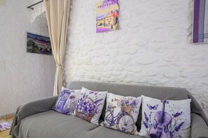 A room with a grey sofa, a white textured wall, and a window with a curtain.