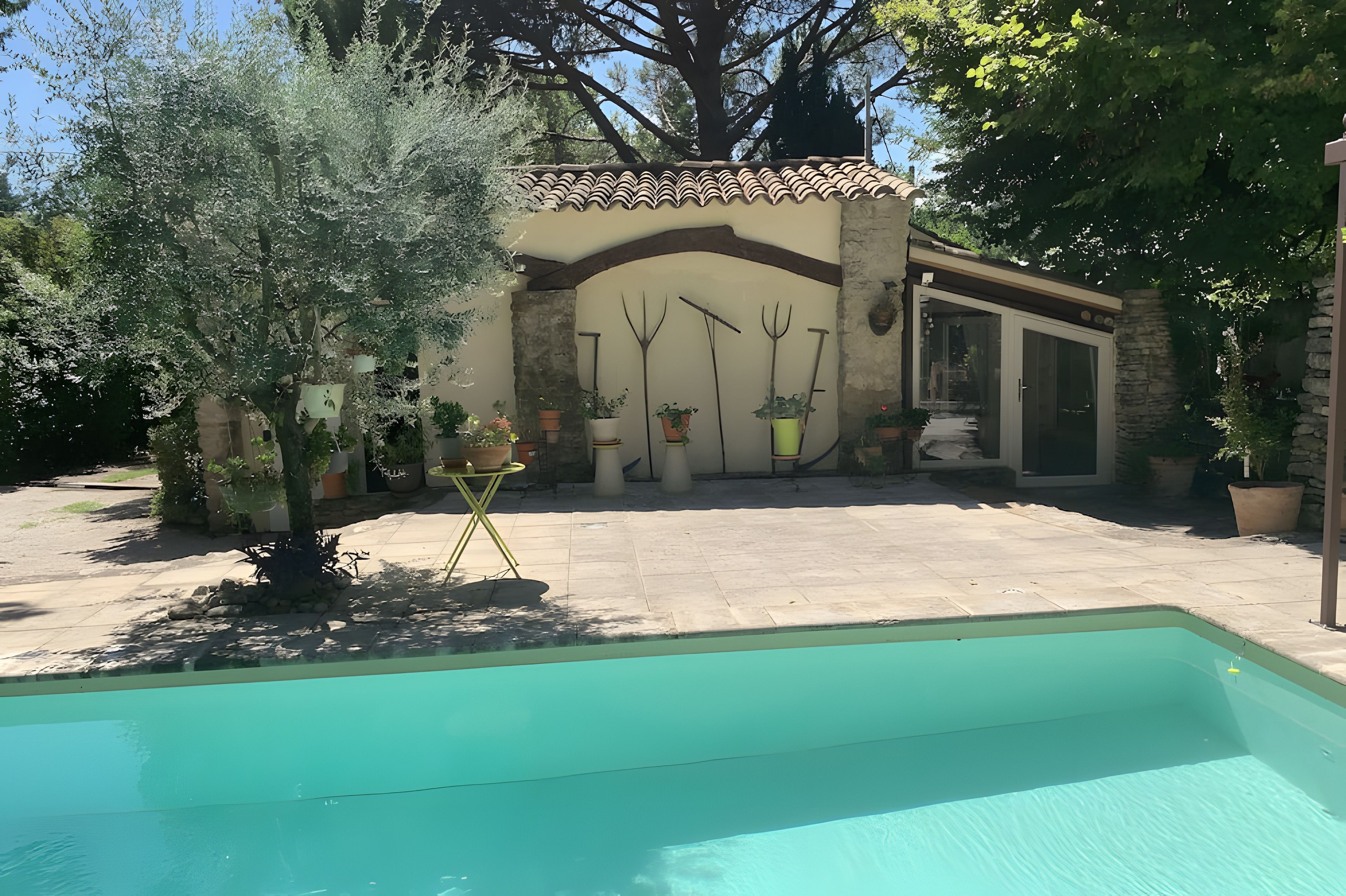 A pool area with a stone patio, a small building with a tiled roof, and various potted plants.