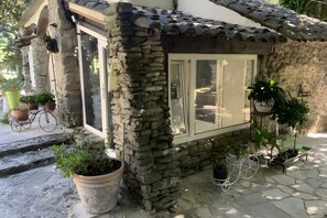 A stone building with a tiled roof, a window, and potted plants. - A fully renovated former sheep barn, located in the petite luberon region (Cheval-Blanc)