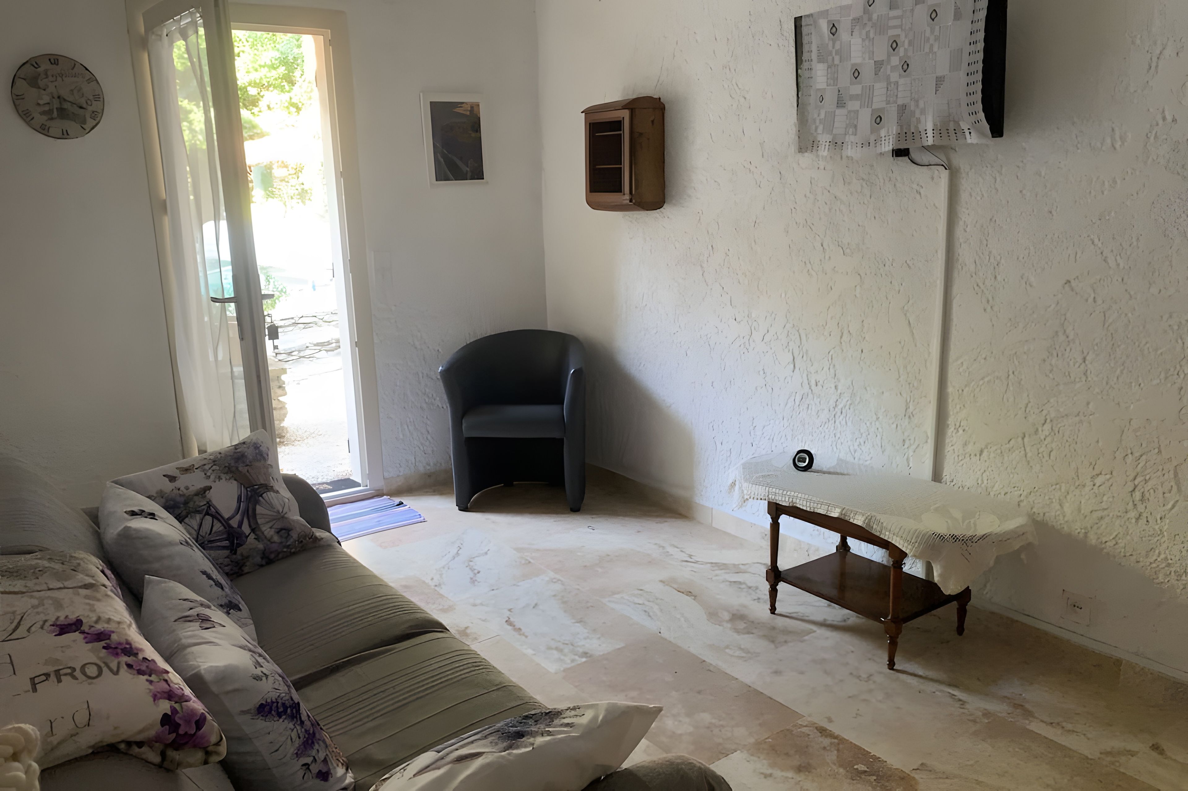 Un salon comprenant un canapé, une petite table, un fauteuil et une porte donnant sur l’extérieur.