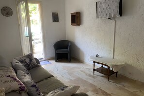 A living room with a sofa, a small table, a chair, and a door leading outside. - A fully renovated former sheep barn, located in the petite luberon region (Cheval-Blanc)