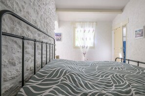 A bedroom with a bed, a window with floral curtains, and a white textured wall.