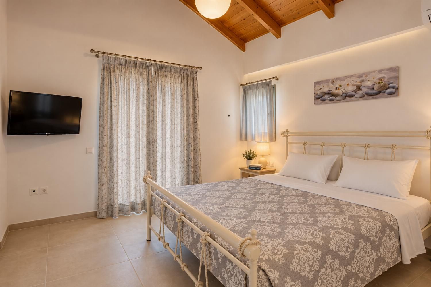 A bedroom with a bed, curtains, a television, a nightstand, and a painting on the wall.