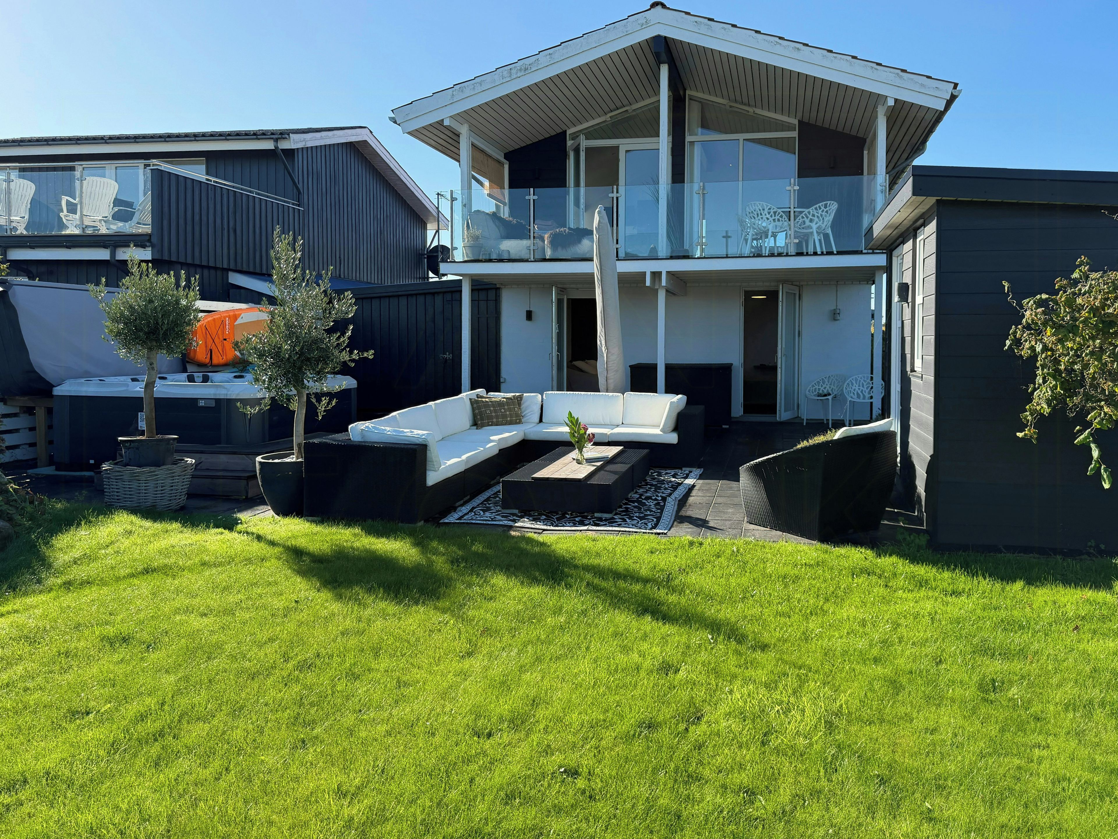 Ein modernes, zweistöckiges Haus mit Balkon, Sitzgelegenheit im Freien und einem gepflegten Rasen.
