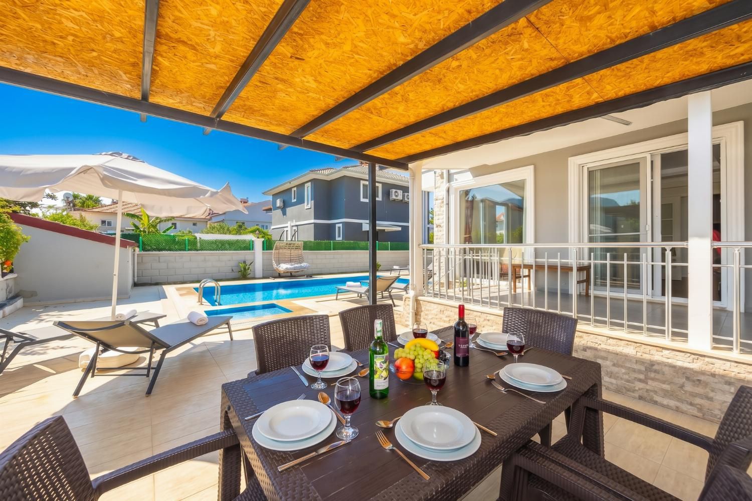 Un área de comedor al aire libre con piscina, mesa dispuesta con platos, vasos y botellas de vino.