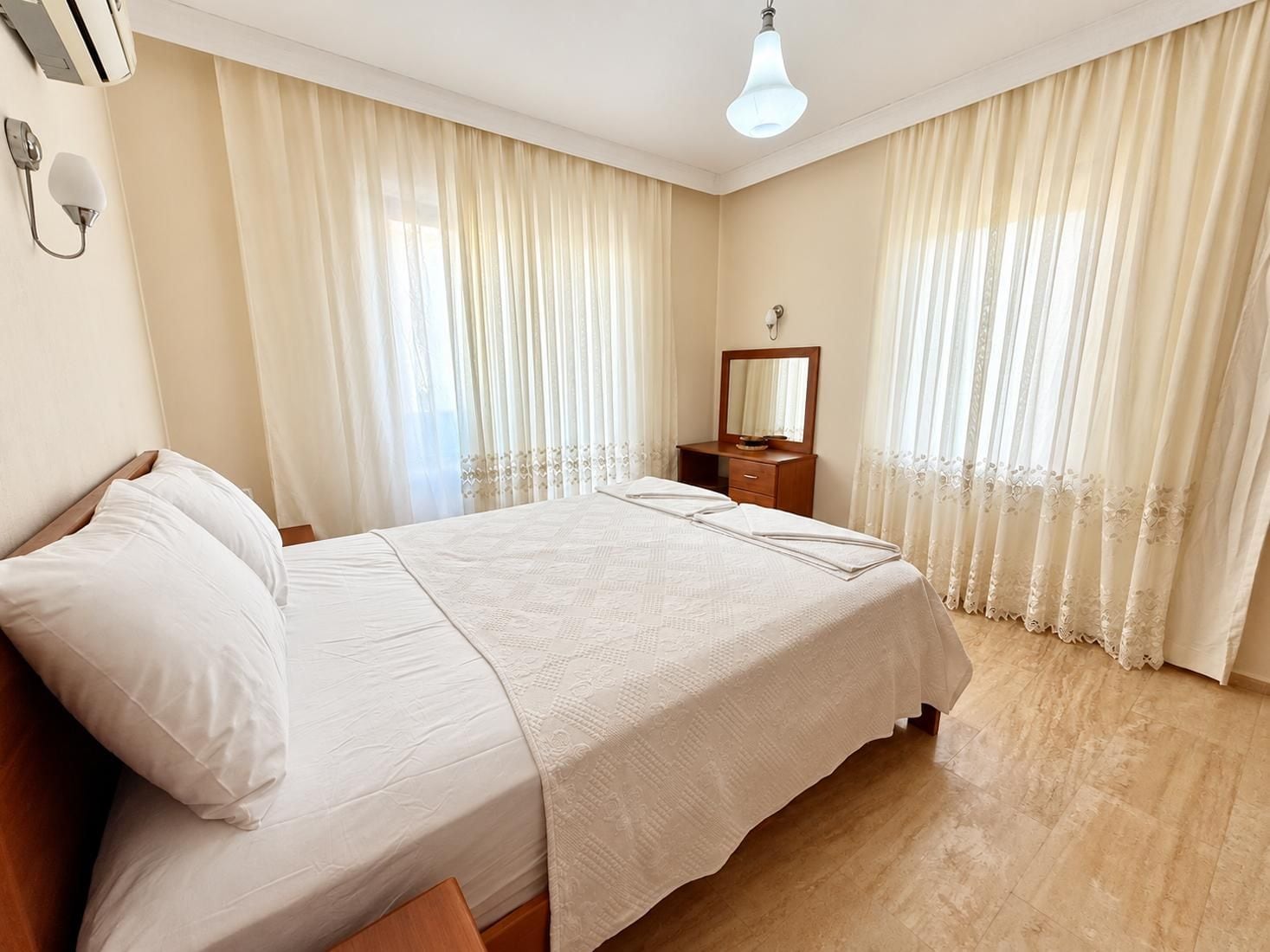 Une chambre d’hôtel avec un lit, une table de chevet, un miroir et des rideaux.