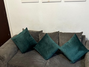A grey sofa with three teal pillows against a white wall with a subtle pattern. - Derby Home Stay, Sleeps 4, Near City Centre (Derby)
