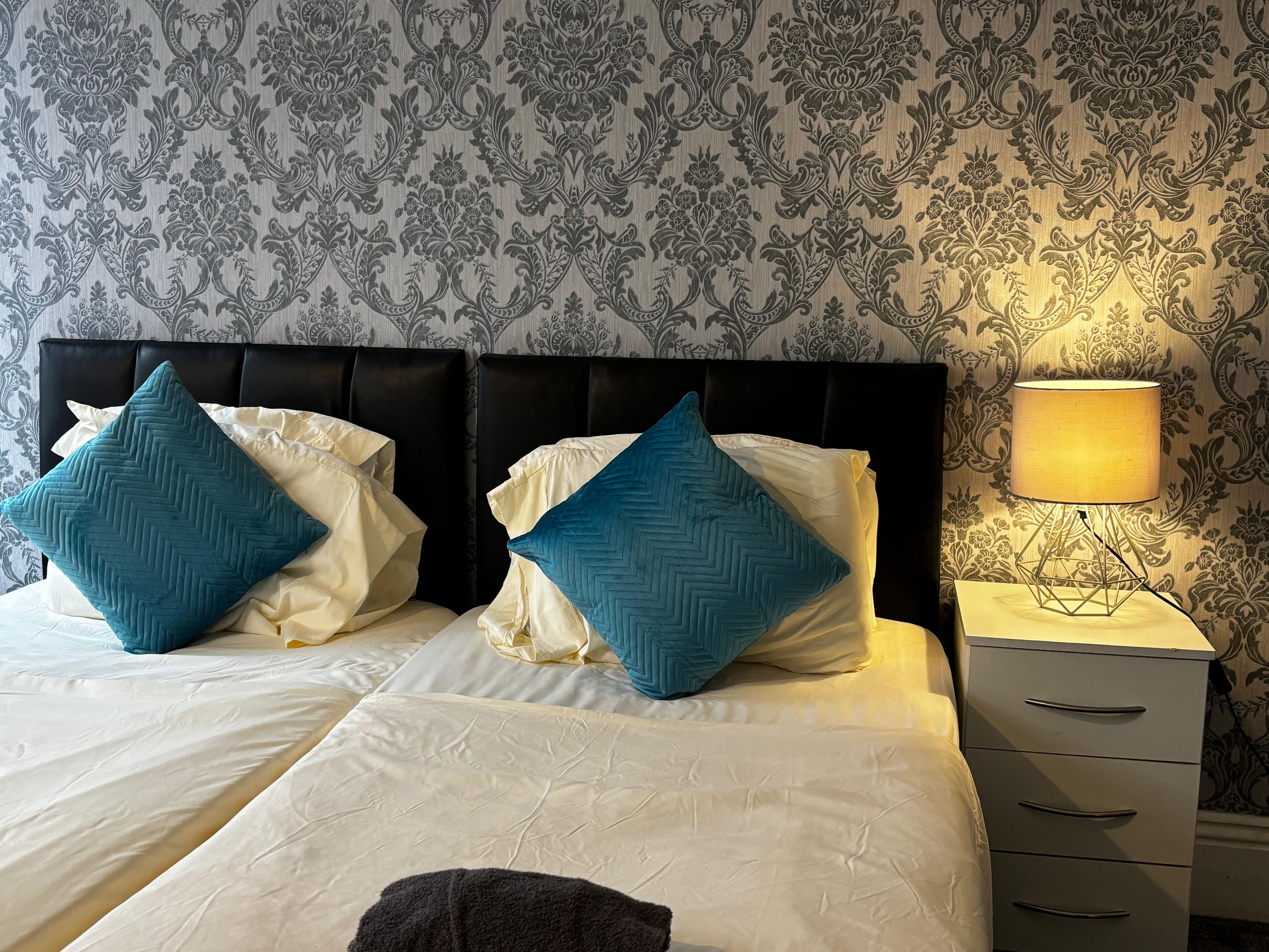 A hotel room with a bed, two pillows, a bedside lamp, and a nightstand.