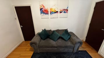 Ein Wohnzimmer mit einem grauen Sofa, zwei grünen Kissen, einem schwarzen Teppich und drei abstrakten Bildern an der Wand.