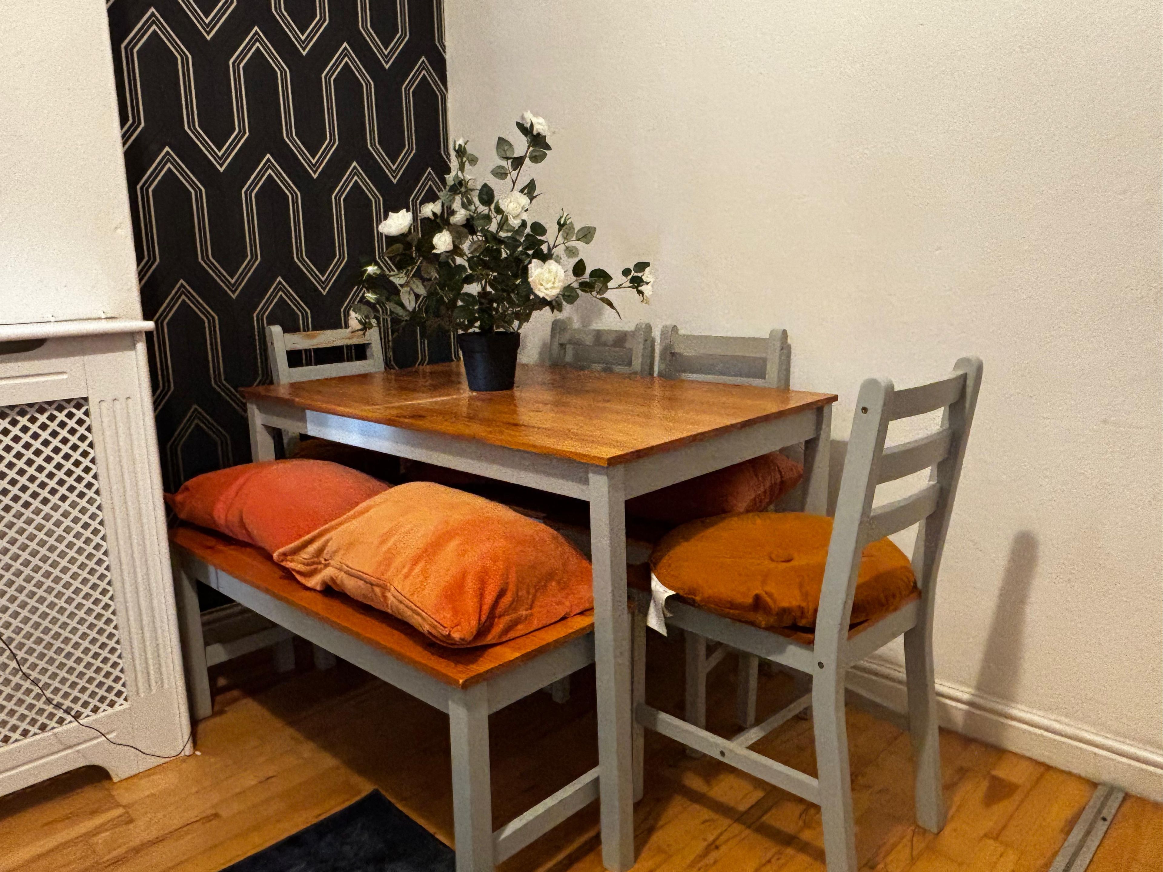 A dining table with four chairs, a potted plant, and a patterned wall.