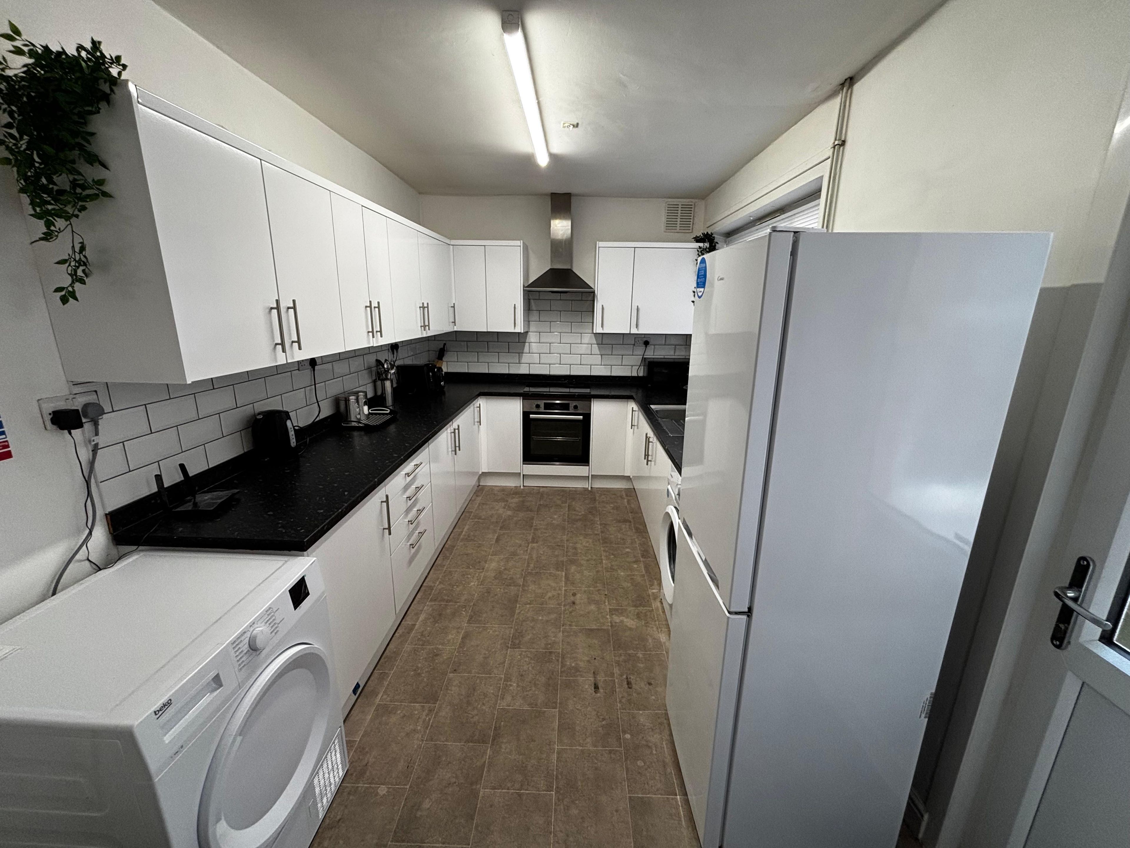 A modern kitchen with white cabinets, a black countertop, a built-in oven, and a washing machine.